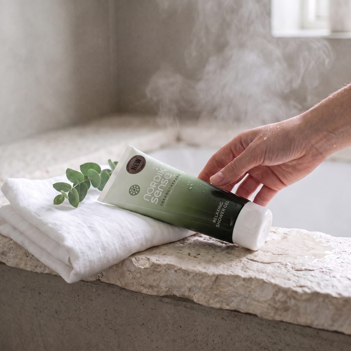 hand legt de nordik sense relaxing shower gel op een natte steen in de stoom